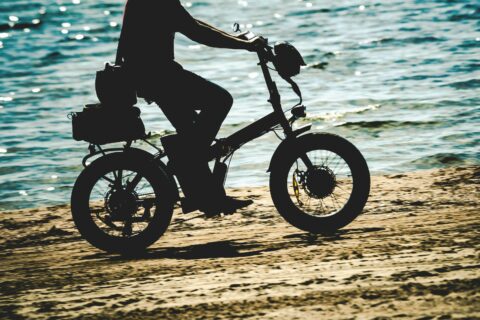 Image of person riding a folding fat tire electric bike on a beack.