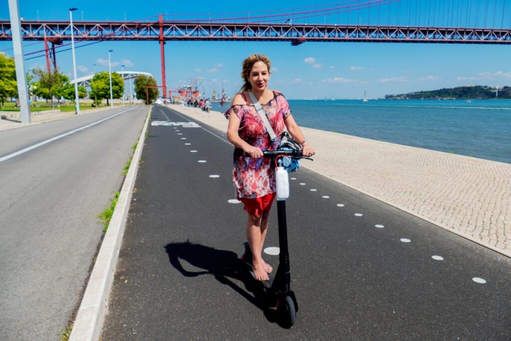 A woman on an electric scooter riding in a bike lane next to the Tagus River in Lisbon