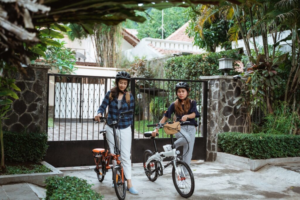 two woman standing in front of a gate holding folding bikes